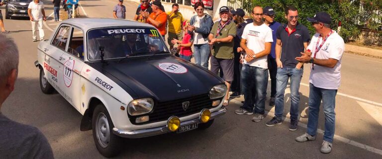 Peugeot 204 Rallye passing the historic Cerda pit buildings during Targa Florio Live in Sicily.