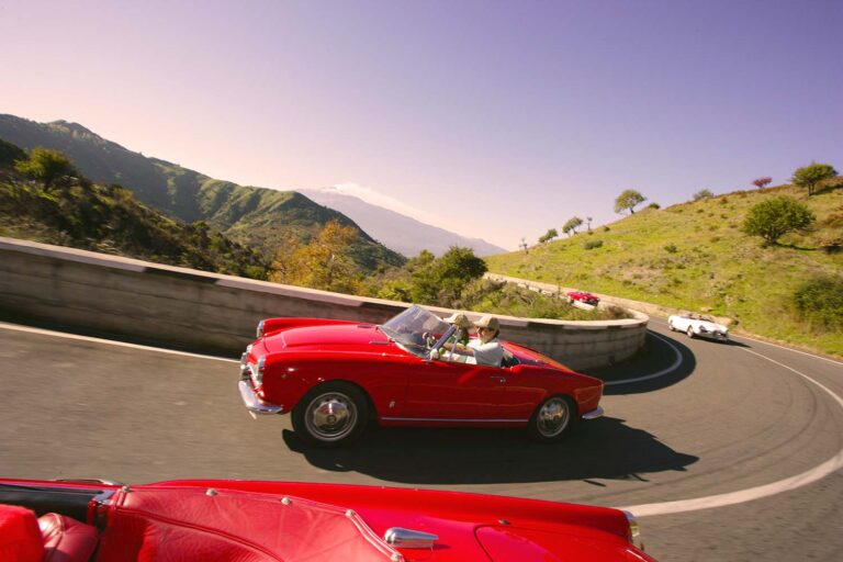 Classic red Alfa Romeo Spider driving through a hairpin on Sicily's legendary Targa Florio route.