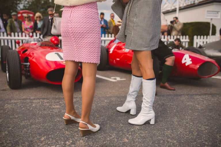 Visitors in period dress beside historic Grand Prix cars at the Goodwood Revival.