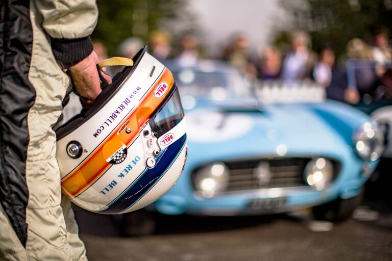 Historischer Rennfahrer mit Helm vor klassischem Ferrari beim Goodwood Revival.