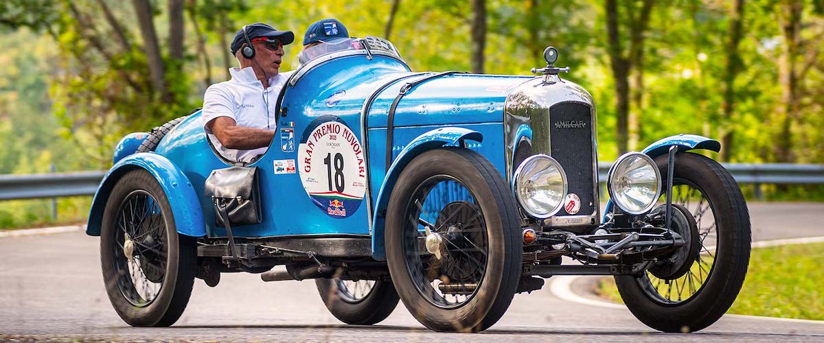 Blauer Amilcar Vorkriegs-Sportwagen mit Startnummer 18 beim Gran Premio Nuvolari auf einer italienischen Landstraße.