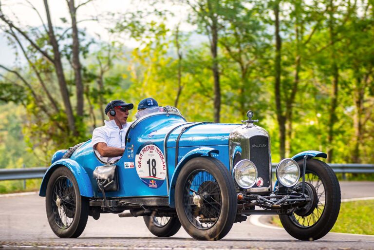 Blue Amilcar sports car on a winding country road during the Gran Premio Nuvolari.