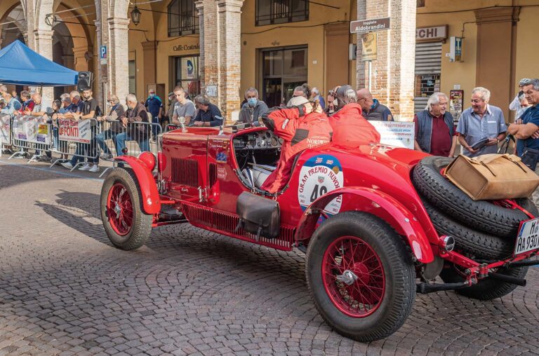 Pre-war sports car driving through a historic Italian town during the Gran Premio Nuvolari.