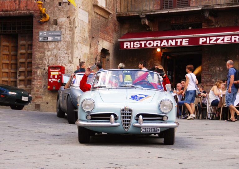 Alfa Romeo Giulietta Spider driving through a historic Italian town during the Gran Premio Nuvolari.
