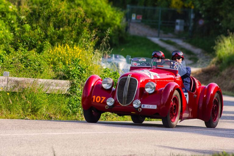 Historic red roadster driving through the Italian countryside during the Mille Miglia.