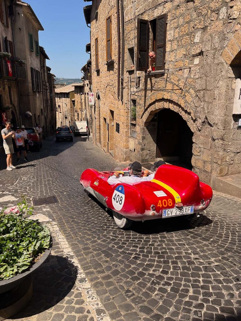 Classic red Ferrari driving through a medieval Italian town during the Mille Miglia.