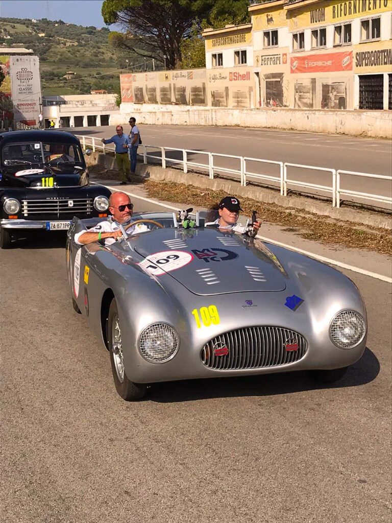 Silver Siata Daina Sport Spider at Targa Florio Live in front of the historic Cerda pit buildings in Sicily.